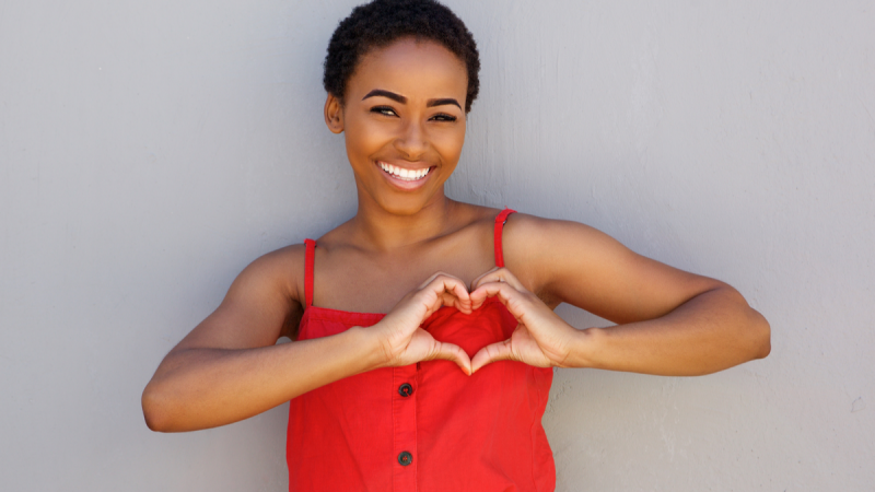 Smiling woman in red tank top holds her hands in heart shape